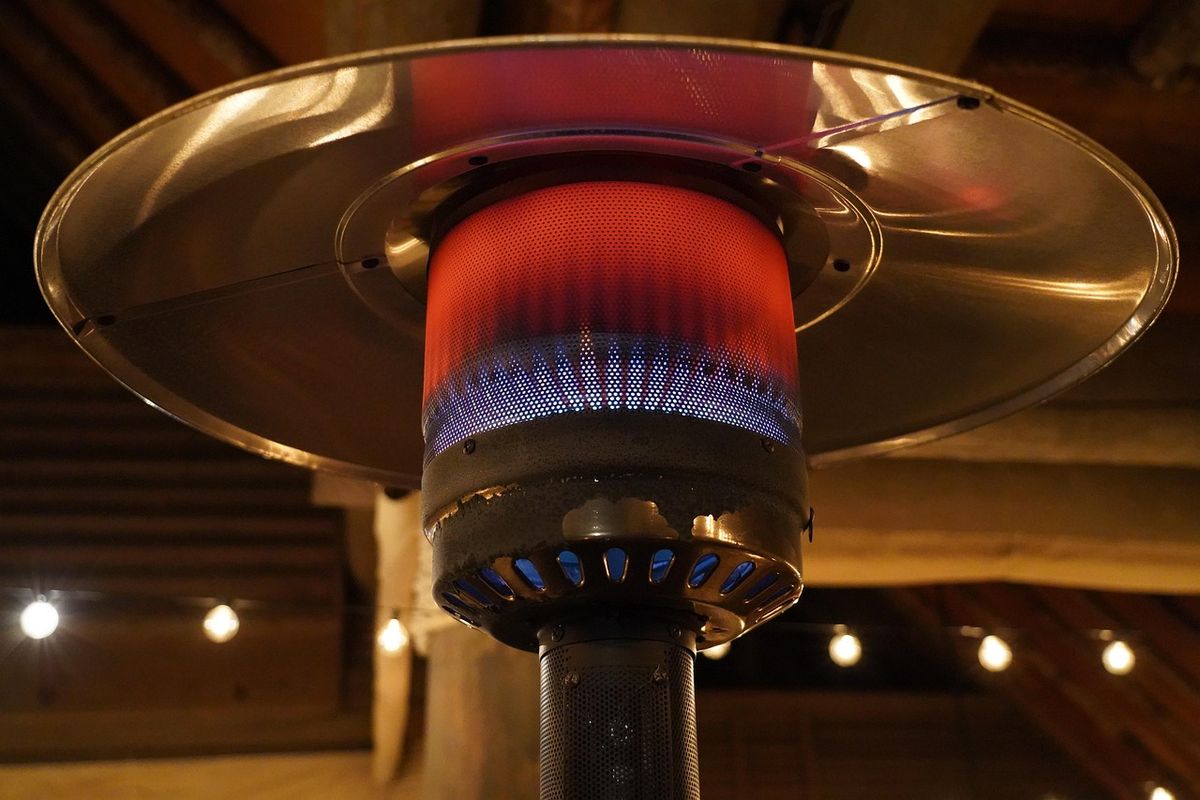 Detalle de una seta de calor de gas encendida, con la llama azul bajo el reflector